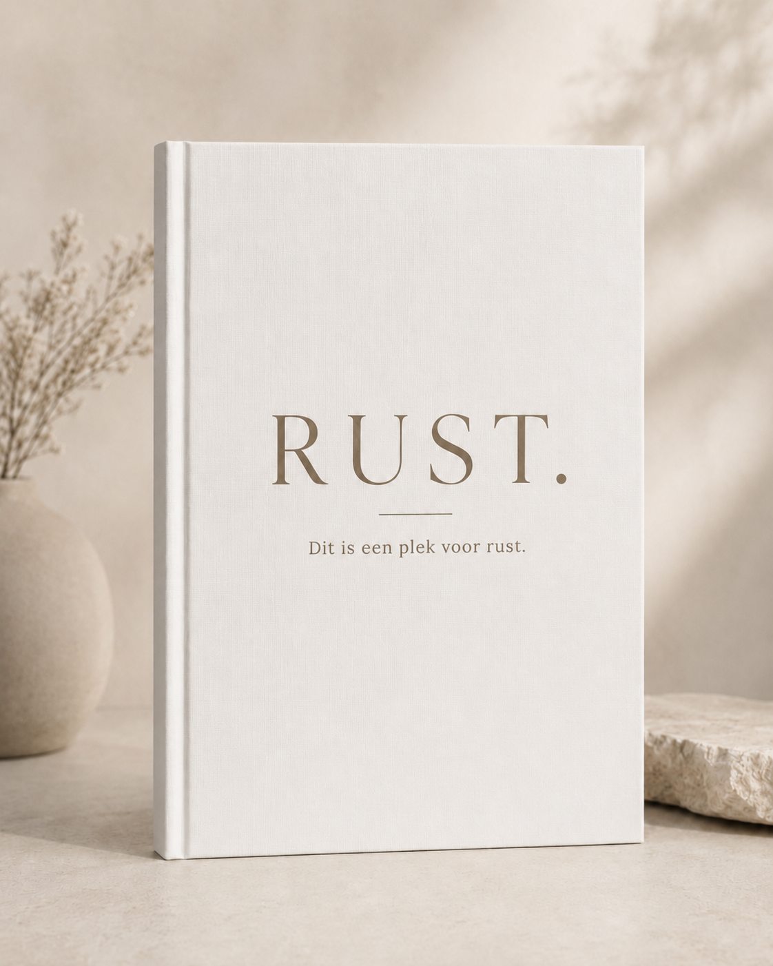 Boek met de titel Rust naast een vaas met droogbloemen op een zandkleurige ondergrond